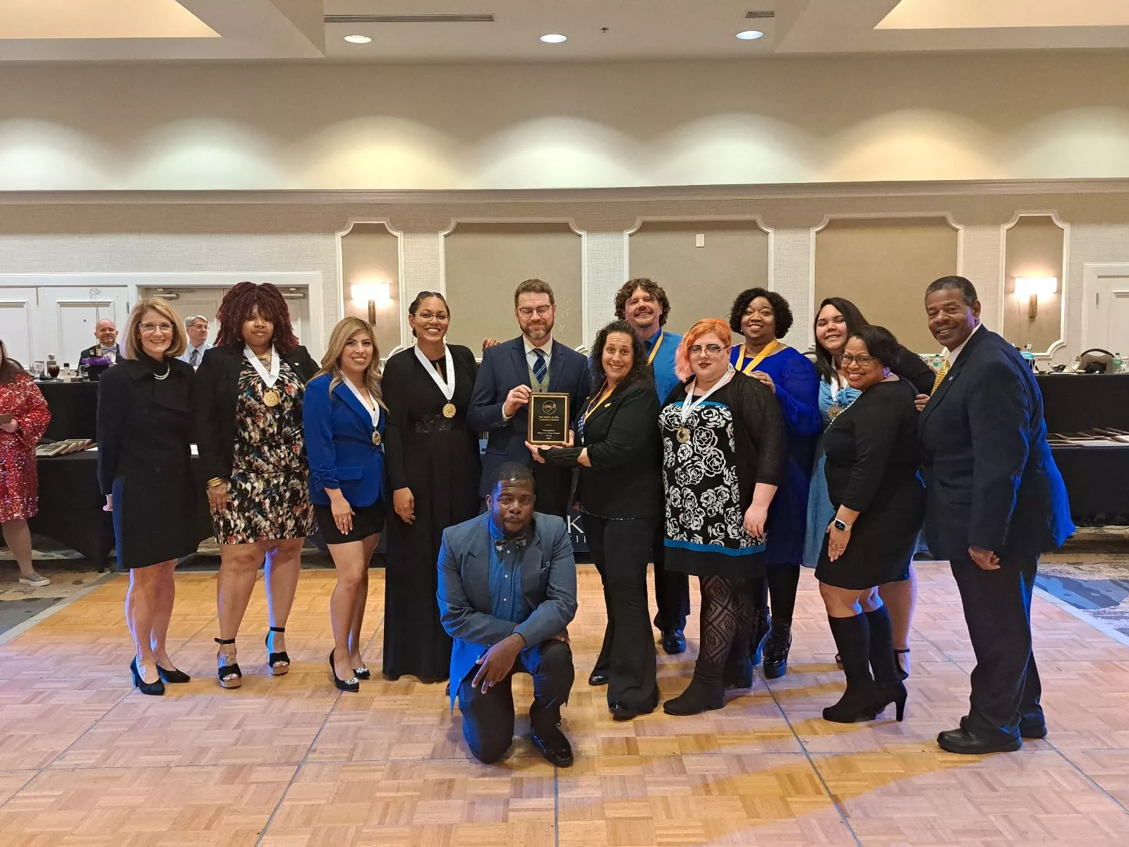 Phi Theta Kappa standing with MTC President and staff holding award and smiling in a ballroom.