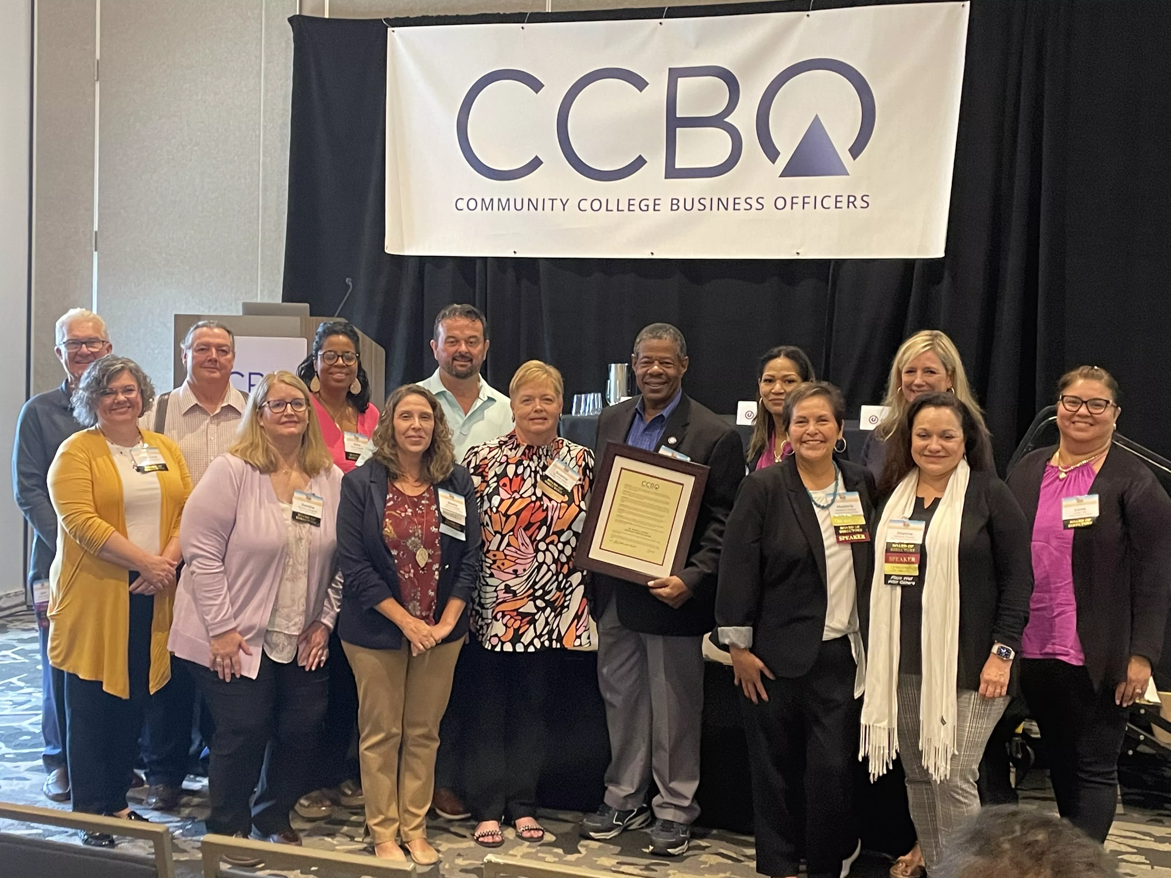 Dr. Ronald L. Rhames standing with The Community College Business Officers holding a certificate.