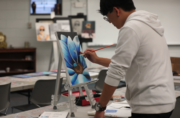 Student painting a picture of a blue flower