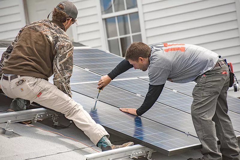 Two workers installing solar panels on a roof