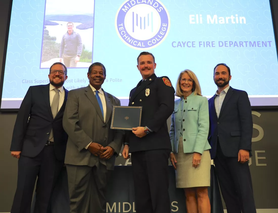President and standing on stage with other professionals while a graduating firefighter holds a certificate