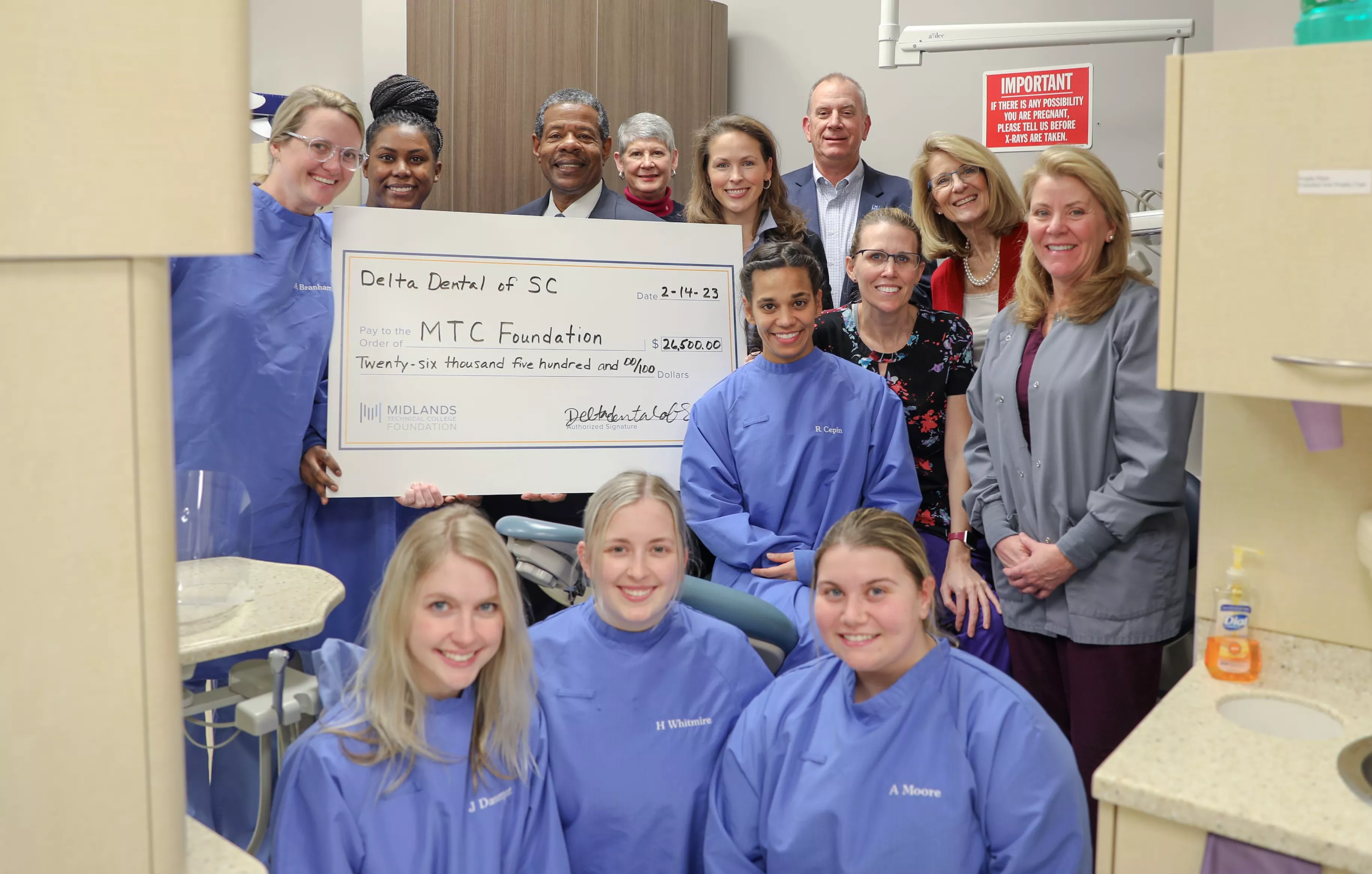 MTC offcials and dental students standing in a dental lab holding large check and smiling
